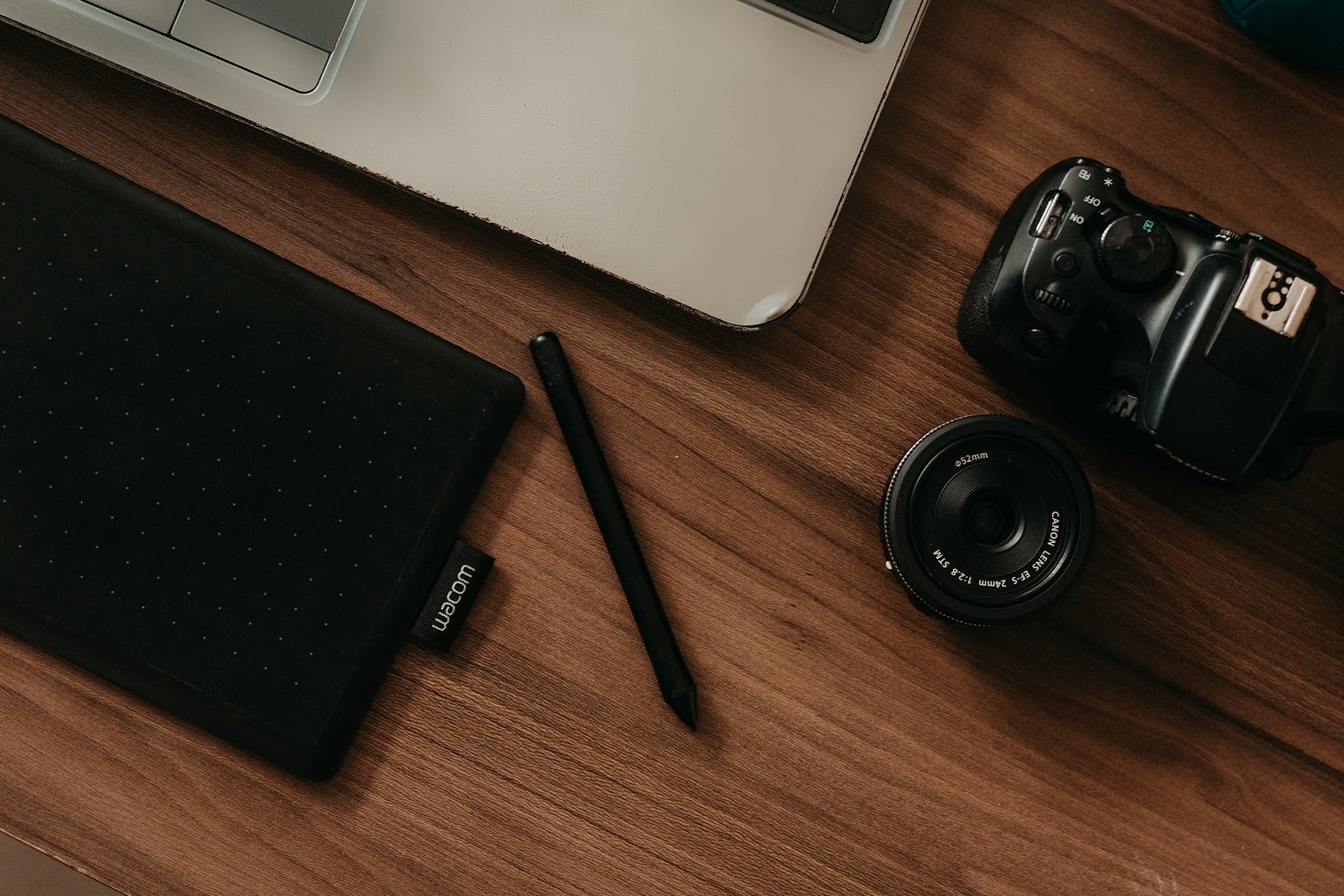 Laptop, graphics tablet, stylus, and camera gear on wooden desk.